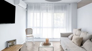 A modern living room with a sofa, a chair, a coffee table, and a TV mounted on the wall. - The Little Bondi Base (Bondi Junction)