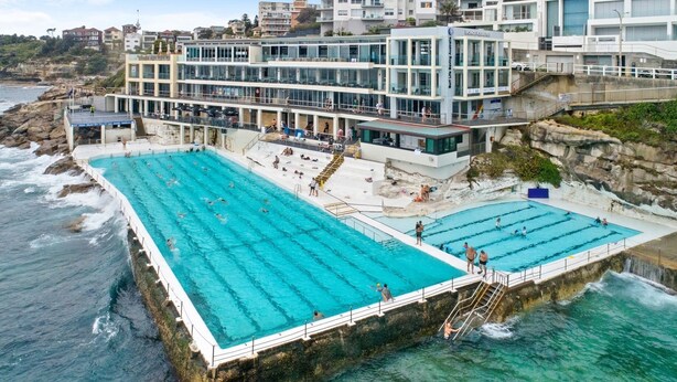 A coastal hotel with two large swimming pools, a rocky shoreline, and a modern building with balconies overlooking the sea. - The Little Bondi Base (Bondi Junction)