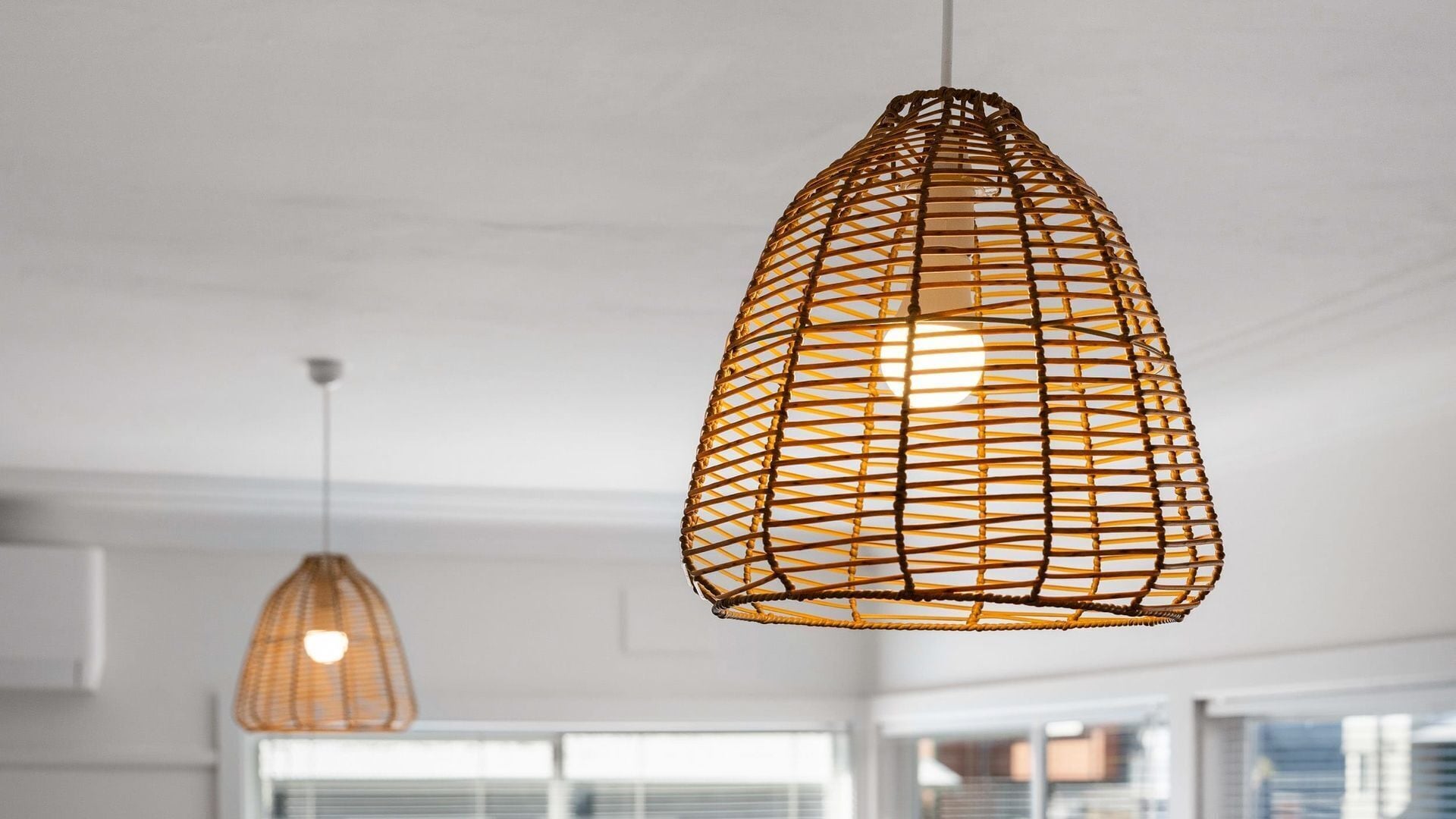 Two hanging wicker pendant lights in a modern interior with white walls and large windows.