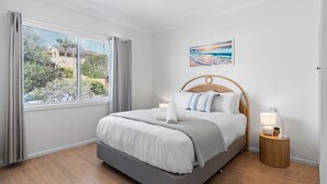 Un dormitorio con cama, ventana con cortinas, lámpara de noche y un cuadro en la pared.