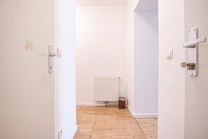Un couloir étroit avec un radiateur, une poubelle et une porte dotée d’une poignée.