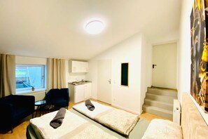 Une chambre d’hôtel avec deux lits, une petite kitchenette, une fenêtre avec des rideaux, un bureau et un escalier.