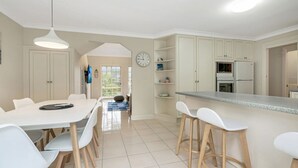 A modern kitchen with white cabinets, a dining area with a table and chairs, and a visible clock on the wall.