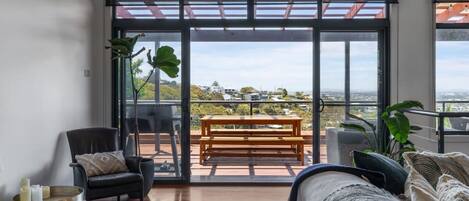 A spacious balcony with a wooden bench, a black leather sofa, and a dining table.