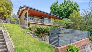 A modern two-story house with a balcony, a stone staircase, and a fenced garden area. - Hilltop Hideaway Merewether Family Escape (Merewether)