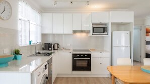 A modern kitchen with white cabinets, a Bosch washing machine, a microwave, and a refrigerator. - Lake Front Home Relax Unwind (Budgewoi)