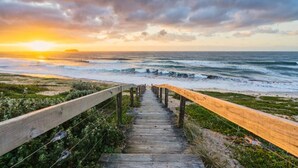 A wooden boardwalk leading to the ocean with a sunset in the background. - Lake Front Home Relax Unwind (Budgewoi)