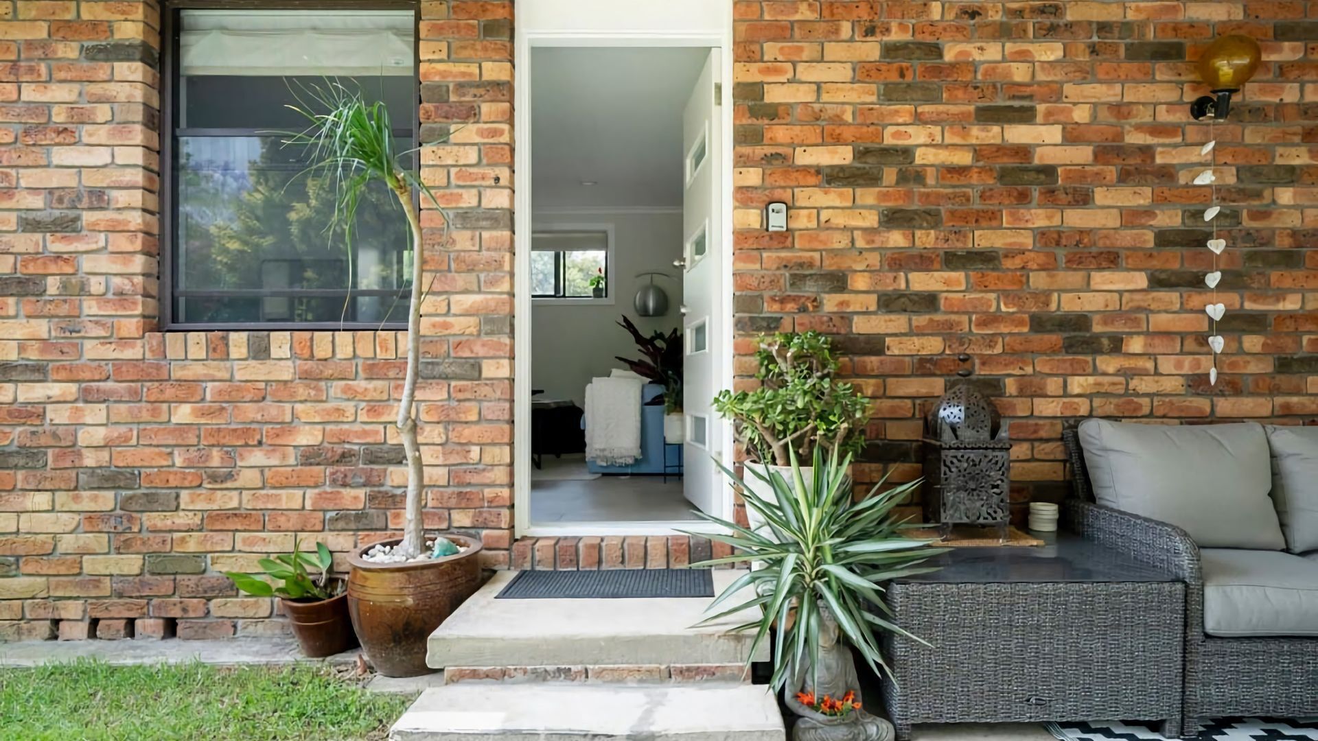 A brick exterior with a glass door entrance, outdoor seating area, and potted plants.
