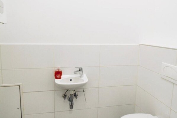 A bathroom with a white sink, a toilet, and a red soap dispenser.