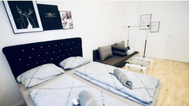 A room with a bed, a bedside table, a lamp, and wall art. - 3B Bedroom Apt, Up to 9P ; Only 10 Min to Augarten (Vienna)