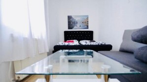 A modern living room with a glass coffee table, a sofa, and a bed with a headboard. - 3B Bedroom Apt, Up to 9P ; Only 10 Min to Augarten (Vienna)