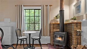 A cozy room with a fireplace, a table with two chairs, and a window with curtains. - Romantic Tricklebeck Spa Cottage (Blackheath)