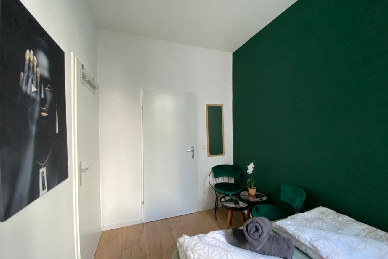 A room with a bed, a chair, a small table with a plant, and a door.