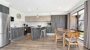 A modern kitchen with grey cabinetry, a stainless steel refrigerator, and a wooden dining table with chairs. - Hitters Paradise Stay Play (Salamander Bay)