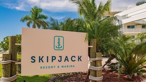 Une enseigne pour le complexe hôtelier et le port de plaisance Skipjack, avec un logo, entourée de palmiers et d’une clôture en bois.