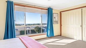 Een kamer met een groot raam, een bed met een roze deken en een deur.