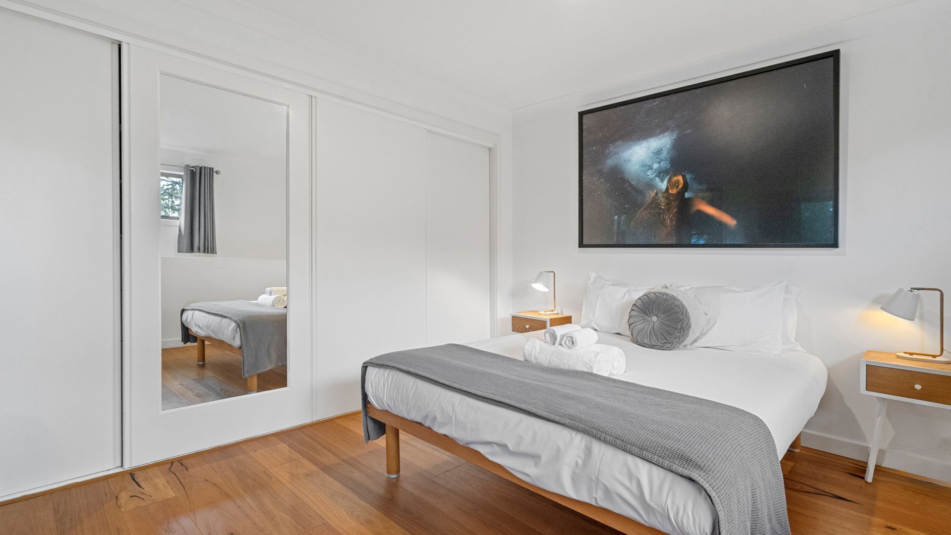 Een moderne slaapkamer met een groot bed, een nachtkastje, een spiegel en een schilderij aan de muur.