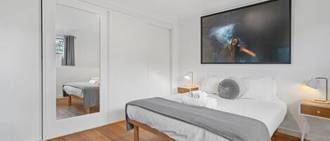 Een moderne slaapkamer met een groot bed, een nachtkastje, een spiegel en een schilderij aan de muur.