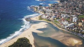 An aerial view of a coastal town with beachfront properties, a sandy beach, and a mix of residential and commercial buildings.
