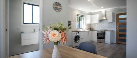 A modern kitchen with a wooden table, a vase of flowers, a washing machine, and a stove.