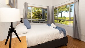 A bedroom with a bed, a lamp on a tripod, and large windows with curtains. - Beachfront Bliss Broulee (Broulee)