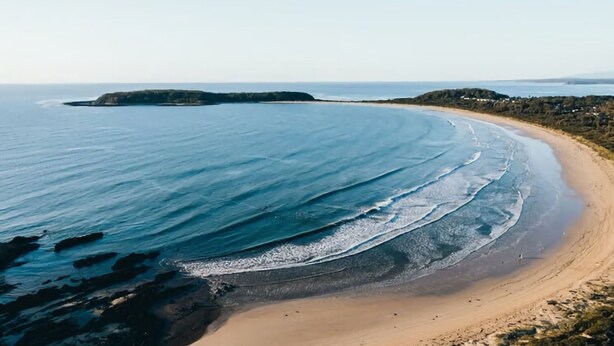 A coastal landscape with a sandy beach, calm sea, and a distant island. - Beachfront Bliss Broulee (Broulee)
