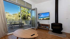 A living room with a wooden table, a TV on the wall, a fireplace, and a sliding glass door leading to a balcony. - Beachfront Bliss Broulee (Broulee)