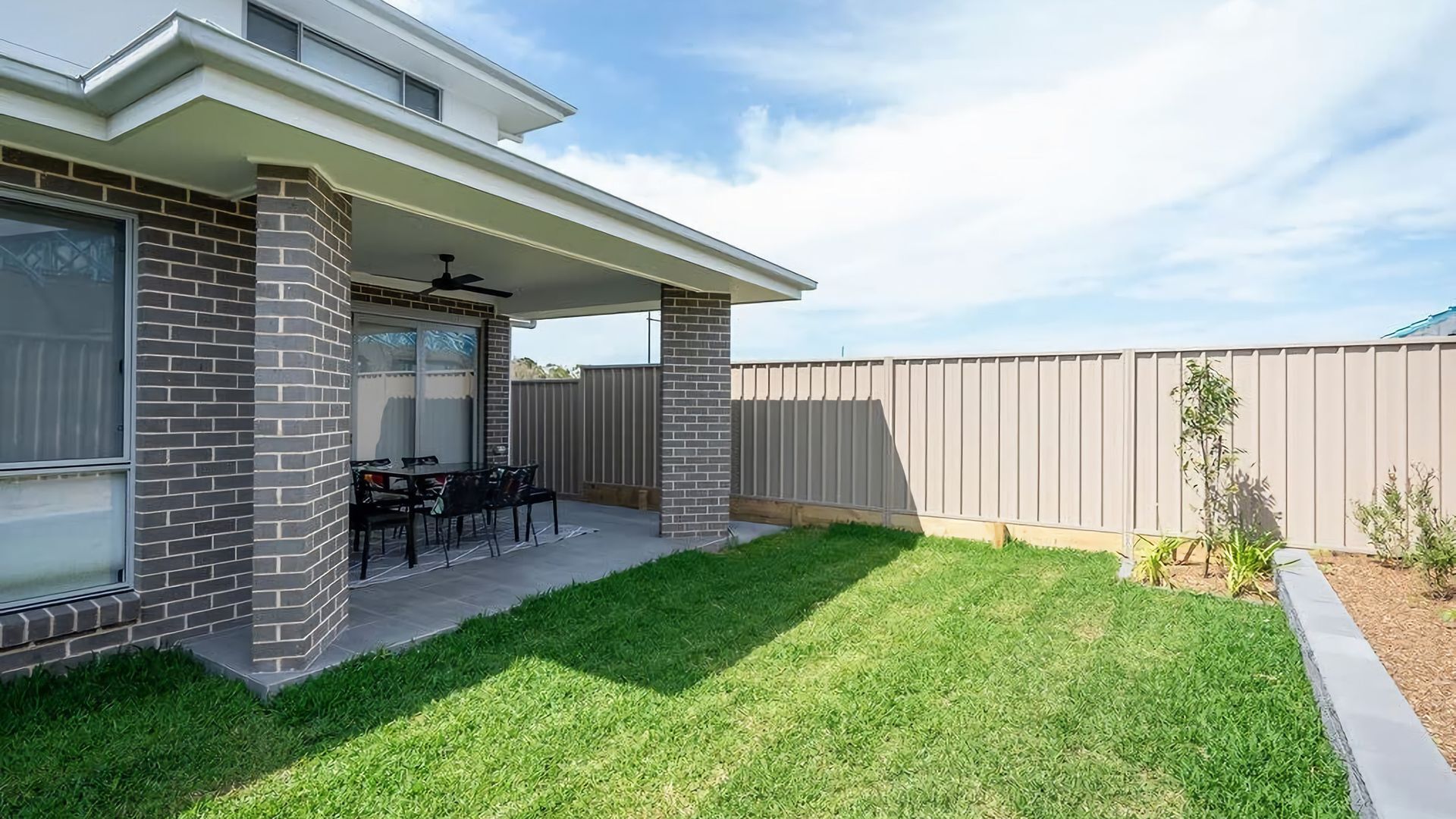 A residential backyard with a patio, a covered seating area, and a fenced yard.