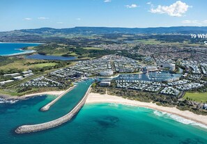 Vista aerea di una località balneare con un porto turistico, spiaggia e edifici a terrazze.