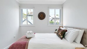 A bedroom with a bed, two windows, a wall decoration, and a red patterned bedspread.