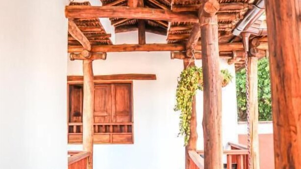 A covered outdoor corridor with wooden beams and columns, a tiled floor, and a hanging plant. - Hotel Tierra Roja  (Barichara)