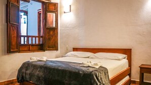 A single bed with a wooden headboard, a dark-colored bedspread, and white pillows. There is a wooden nightstand to the right of the bed. - Hotel Tierra Roja  (Barichara)