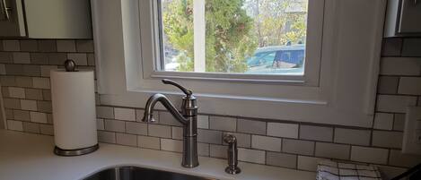 A kitchen with a stainless steel sink, a window above it, and a roll of paper towels on the counter.