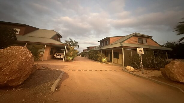 A residential street with houses, a dirt road, and a speed limit sign.