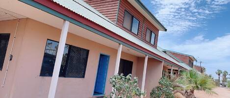 A two-story building with a flat roof, a blue door, and windows with metal grilles.