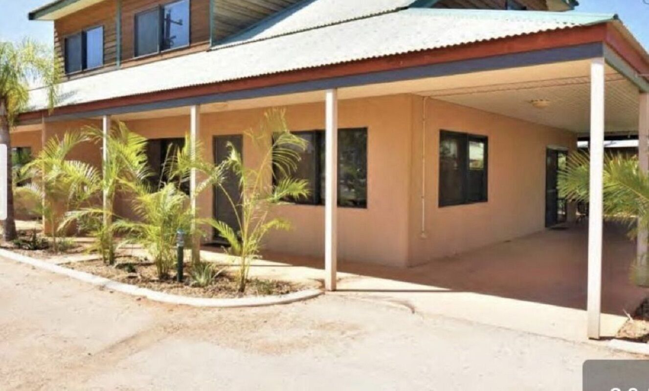 Un edificio de dos pisos con un patio cubierto, palmeras y un cielo despejado.