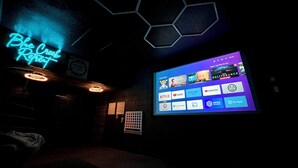Et svagt oplyst rum med et neon-skilt, der viser "Blue Creek Retreat", og en stor skærm, der afspiller forskellige streamingtjenester.