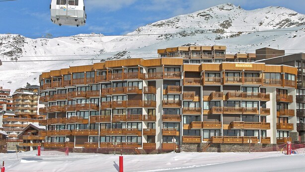 A multi-story hotel with balconies, a ski lift in the background, and snow-covered mountains. - Le Roc de Peclet by Interhome (Val Thorens)