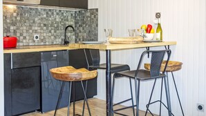 A modern kitchen with a wooden countertop, two bar stools, a red pot, and a wine bottle. - Le Roc de Peclet by Interhome (Val Thorens)