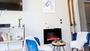 A living room with a flat-screen TV, a fireplace, two blue armchairs, a small table with drinks, and a ski rack against the wall. - Le Roc de Peclet by Interhome (Val Thorens)