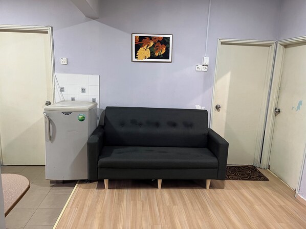 A room with a black sofa, a small white refrigerator, and two doors.