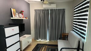 A compact living space with a sofa, a small table, a TV, a wardrobe, and a patterned rug. - Homestay WaDi 2, Apartment with pool near beach (Port Dickson Town)