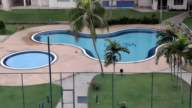 A swimming pool with a curved design, surrounded by palm trees and a grassy area. - Homestay WaDi 2, Apartment with pool near beach (Port Dickson Town)