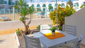A patio with a table and chairs, a hanging lamp, and a view of white buildings in the background.