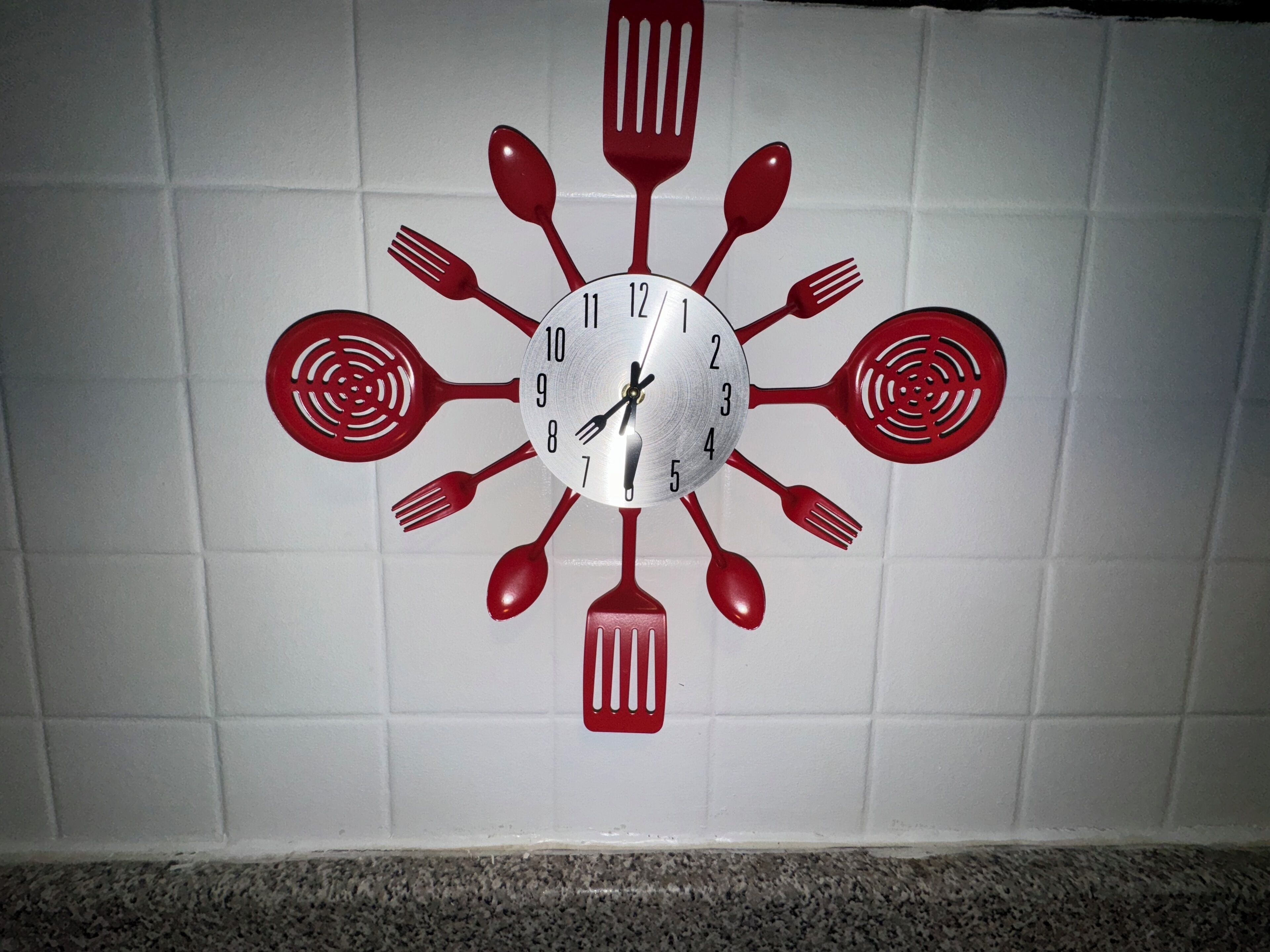 A wall clock with a unique design featuring kitchen utensils as hour markers.
