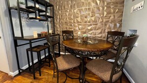 Zona pranzo con tavolo rotondo, sei sedie, parete decorativa e libreria con diversi oggetti.