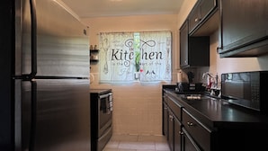 Una cucina moderna con frigorifero in acciaio inossidabile, forno integrato, microonde ed eleganti mobili scuri. Una parete decorativa reca la scritta 'Kitchen is the heart of the home' e un piccolo tappeto ricopre il pavimento.
