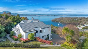 A modern two-story house with a grey roof, surrounded by lush greenery and a view of a lake with boats. - ACACIA WATERS (Taupo)