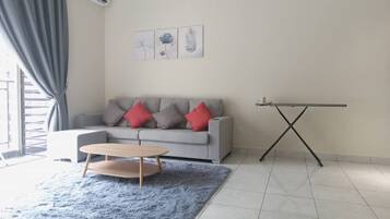 A living room with a grey sofa, red and grey cushions, a round wooden coffee table, a blue shaggy rug, and a black TV stand.