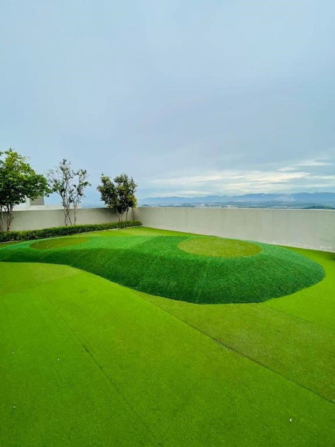 A well-maintained lawn with a circular pattern, a low wall, and a view of distant mountains.
